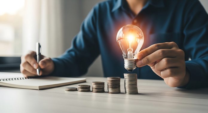 Businessman holding a glowing light bulb over stacked coins on a